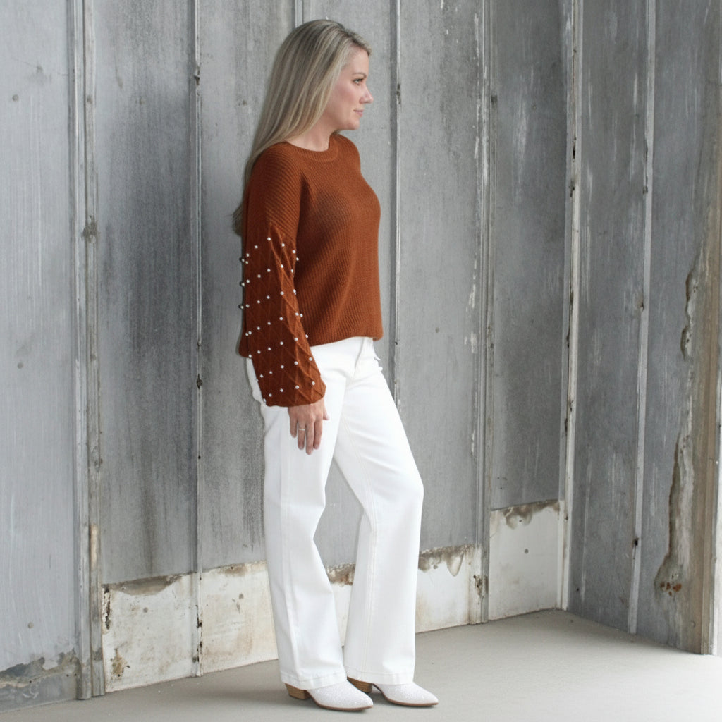 Person lying on a set of wooden stairs wearing a brown sweater and white pants.