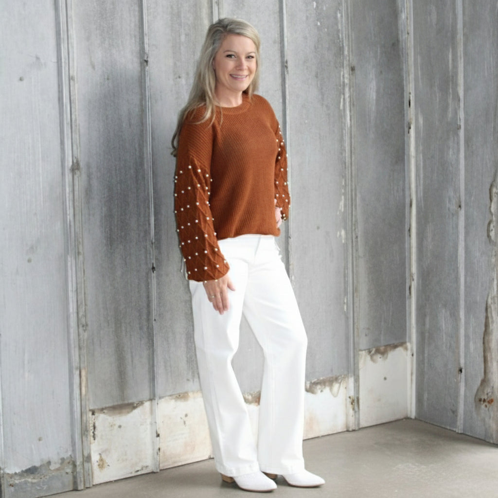 Person wearing a brown sweater with white polka dots and white pants standing on a wooden floor.