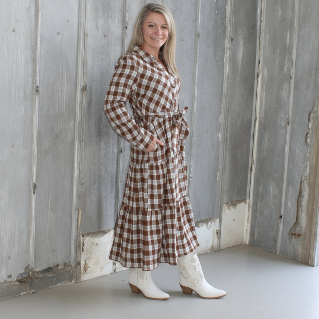 Woman in a checkered dress standing on a wooden deck next to a stone wall.