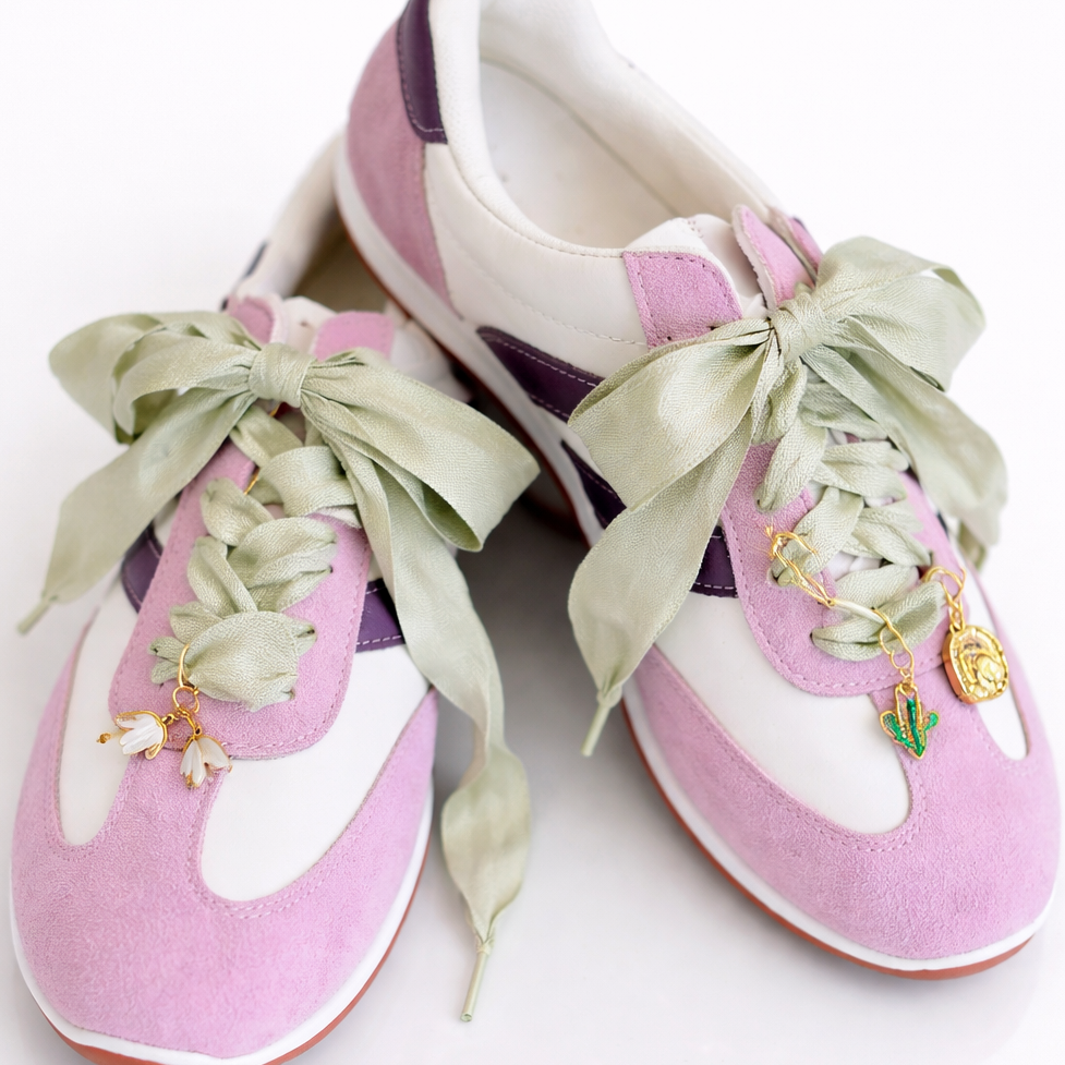Pair of pink and white sneakers with decorative ribbons on a white background
