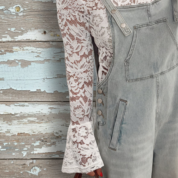 Person wearing a lace top and denim overalls taking a mirror selfie.