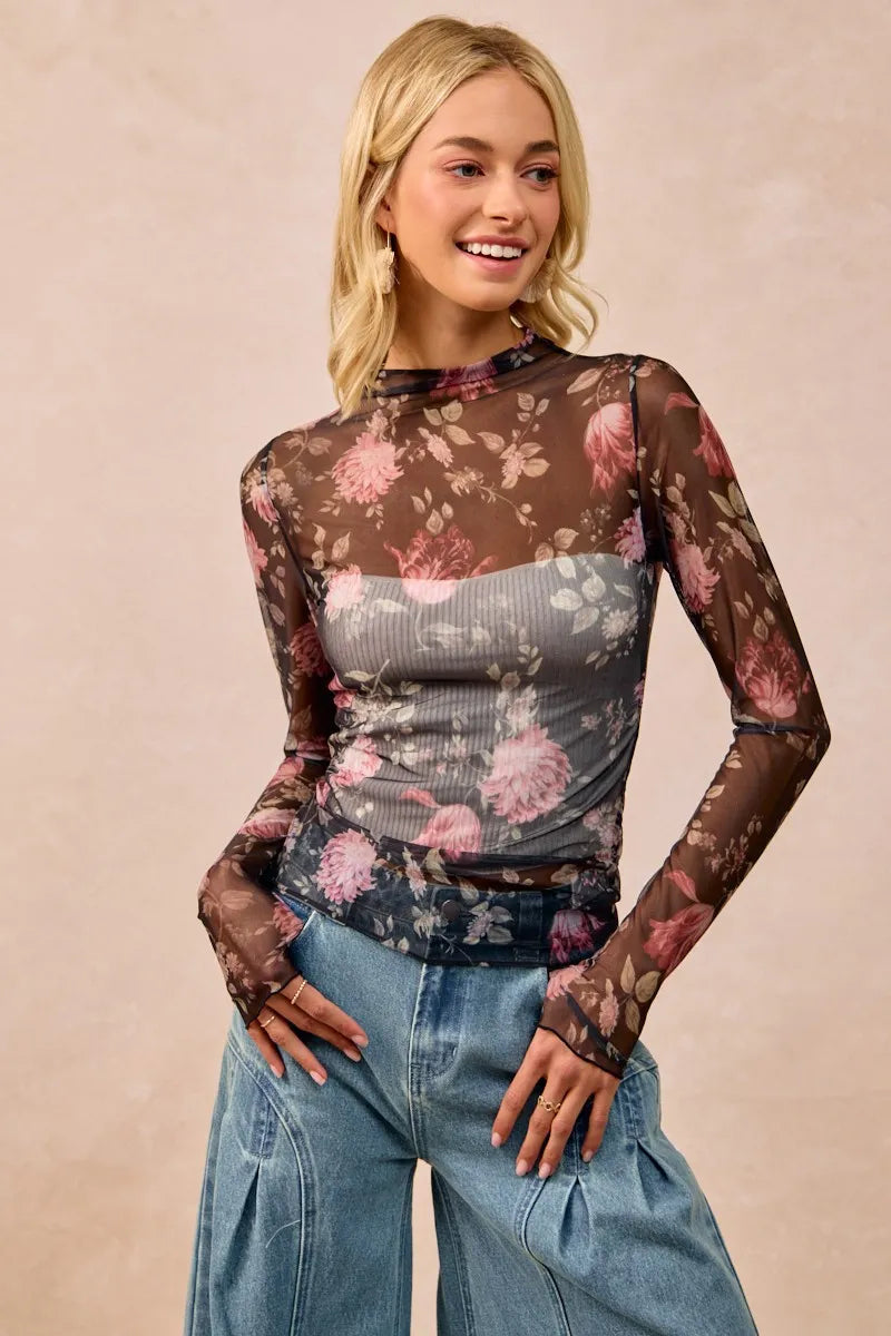 Woman wearing a floral sheer top and jeans on a beige background