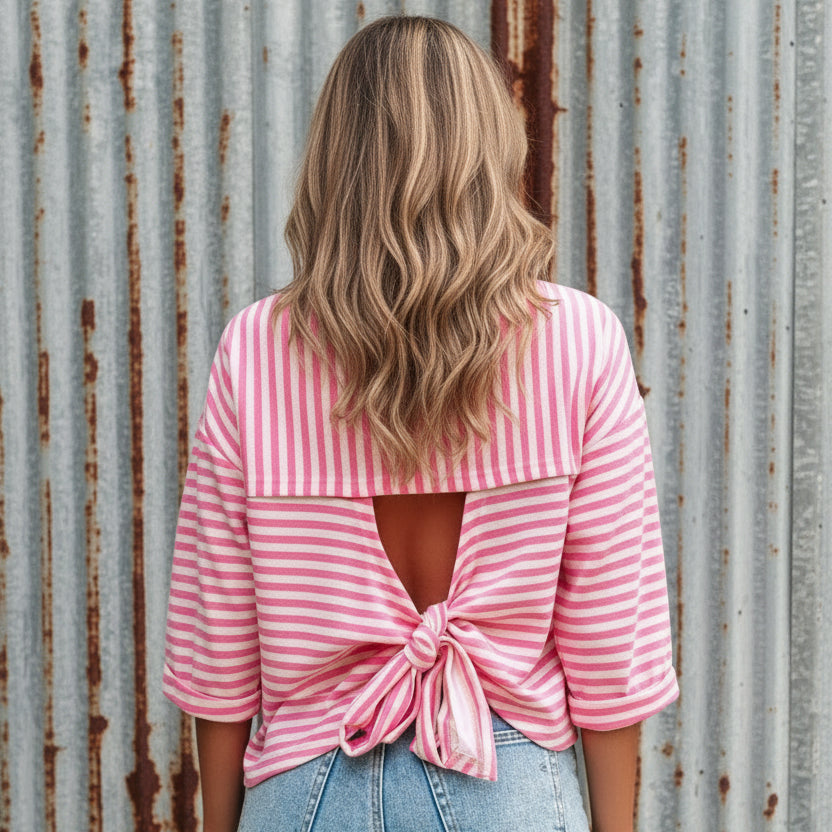 Person wearing a pink and white striped shirt with a knot detail, standing outdoors.