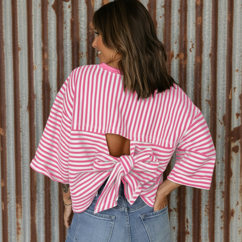 Person wearing a pink and white striped top with a knot detail, paired with blue jeans on a plain background.