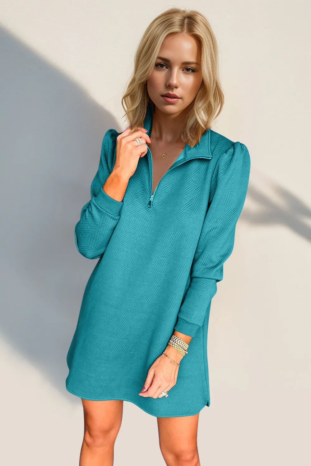 Woman wearing a teal dress against a plain background