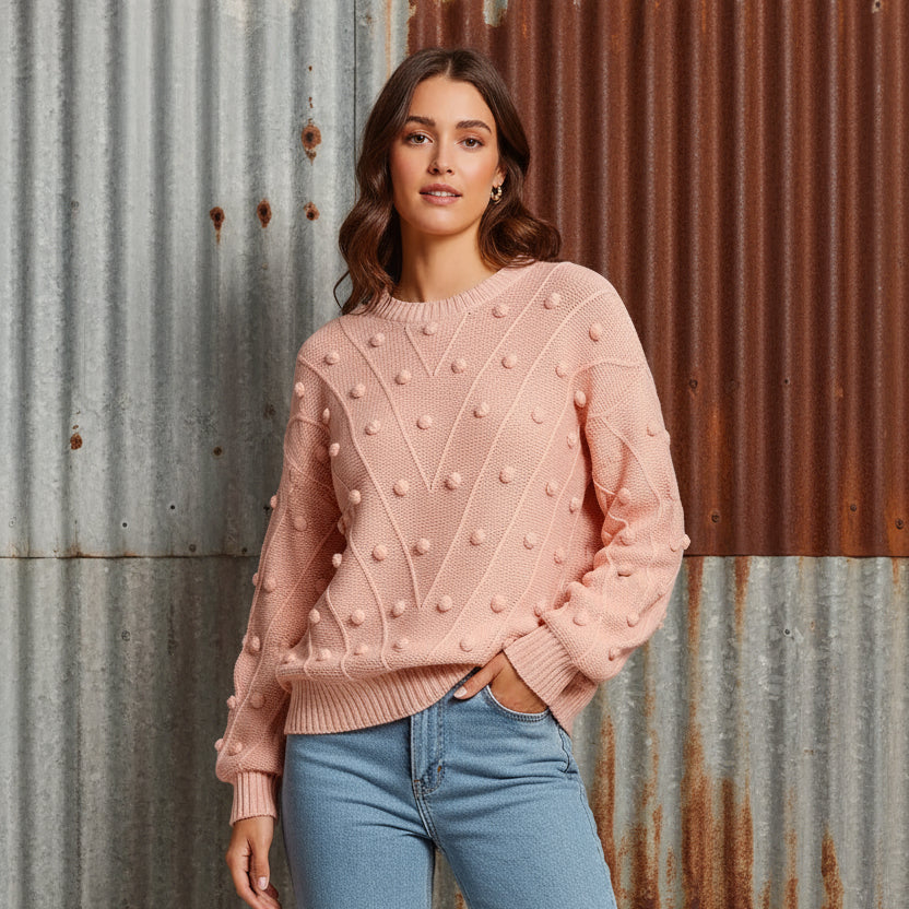 Woman wearing a pink textured sweater with blue jeans on a beige background