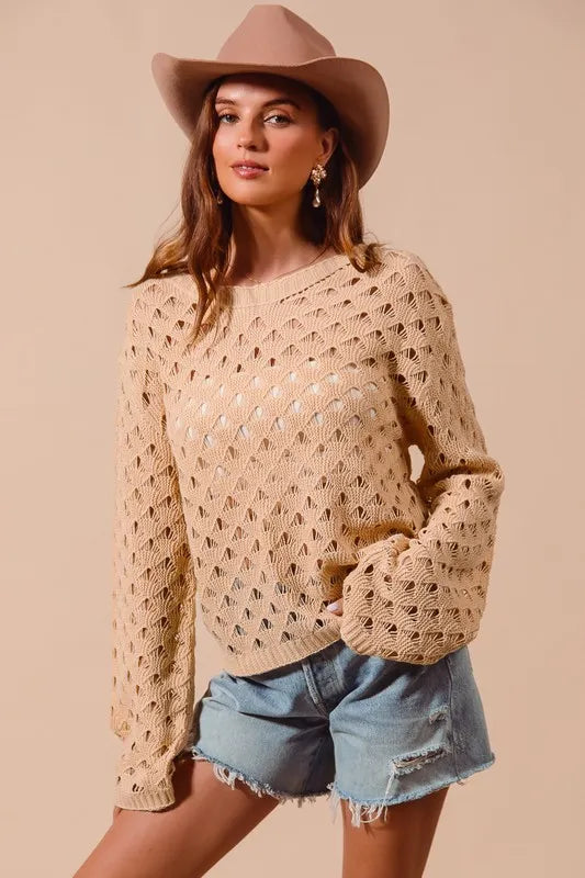 Woman wearing a beige crochet sweater and denim shorts with a beige hat on a beige background