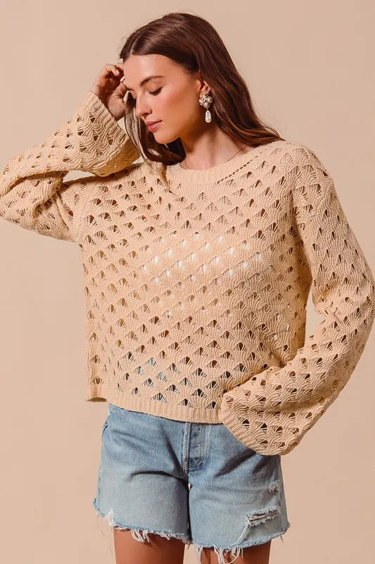 Woman wearing a beige knitted sweater and denim shorts against a beige background