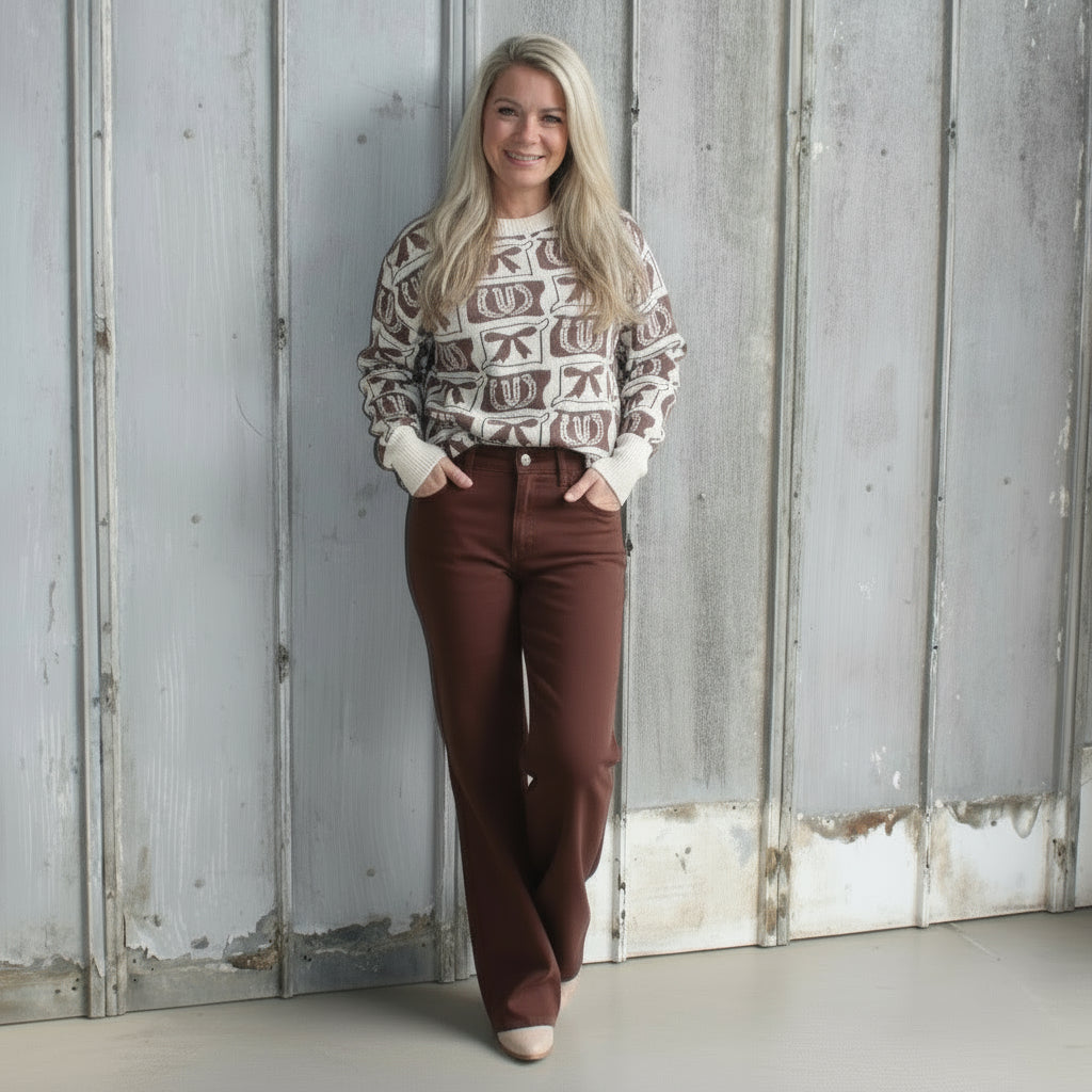 Person wearing a patterned sweater and brown pants standing against a textured wall.