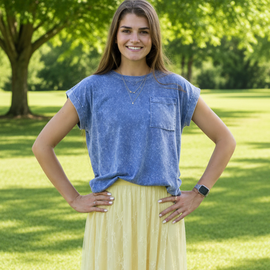 Woman wearing a blue top and yellow lace skirt standing on grass with trees in the background
