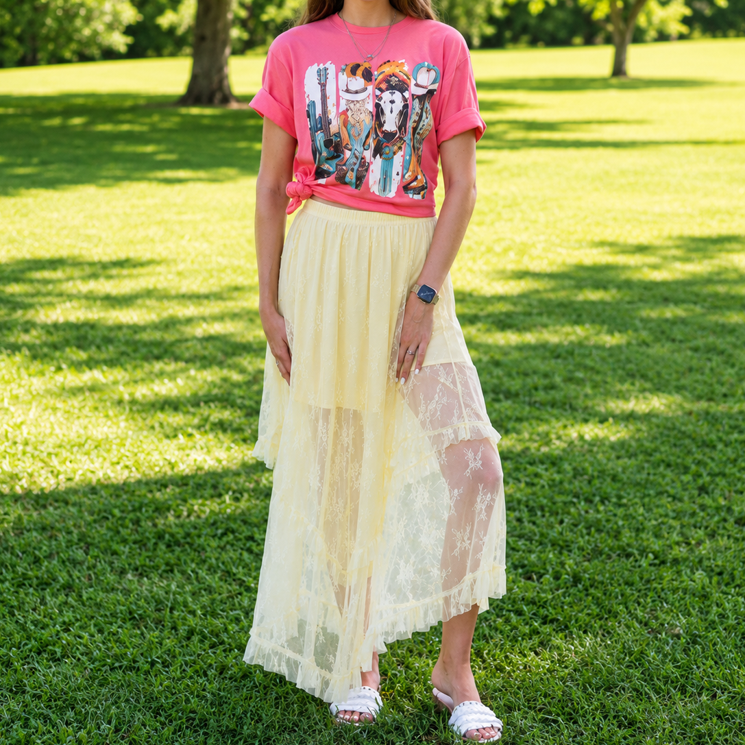 Woman wearing a colorful graphic t-shirt and light yellow skirt standing on grass with trees in the background