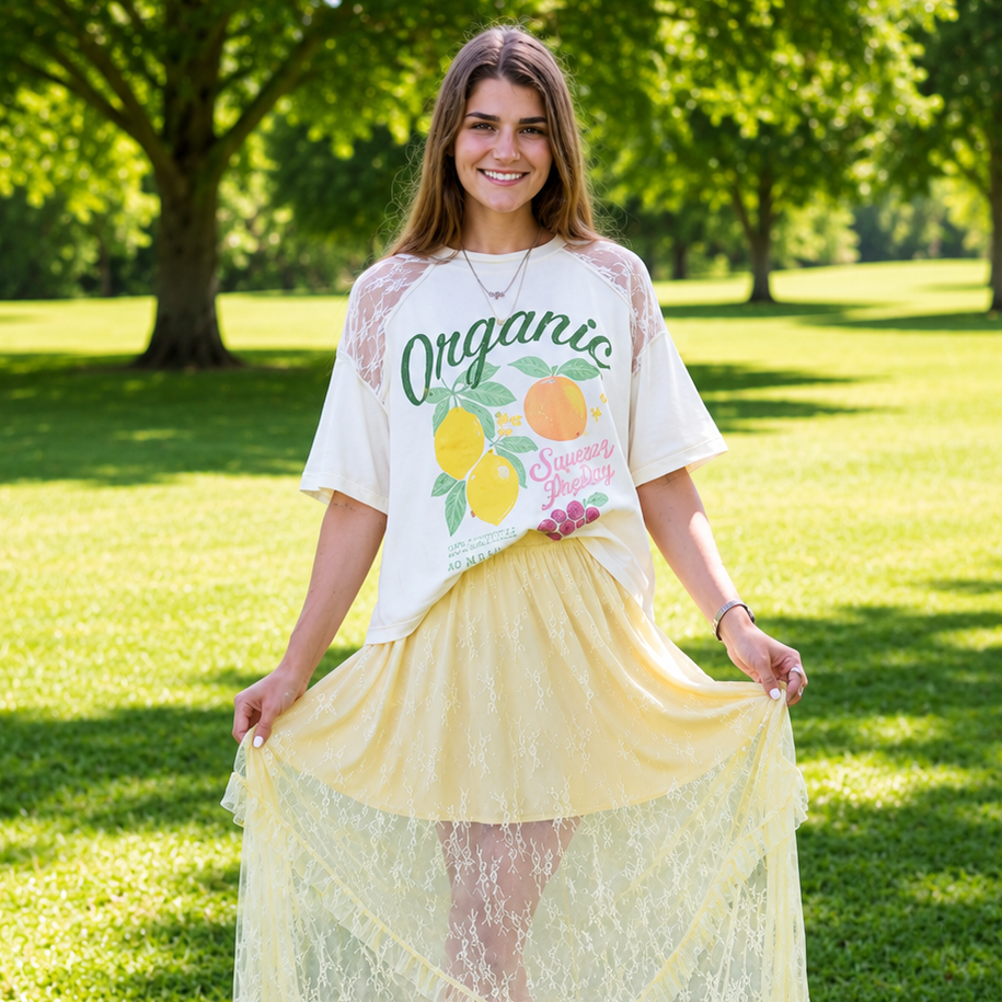 Woman wearing a white t-shirt with graphics and a yellow lace skirt standing in a park.