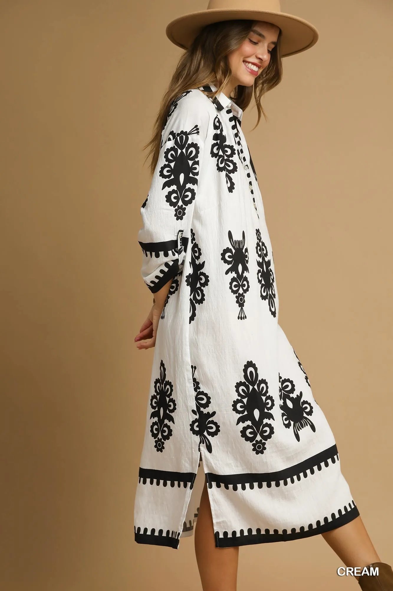 Woman wearing a white dress with black patterns and a beige hat on a beige background