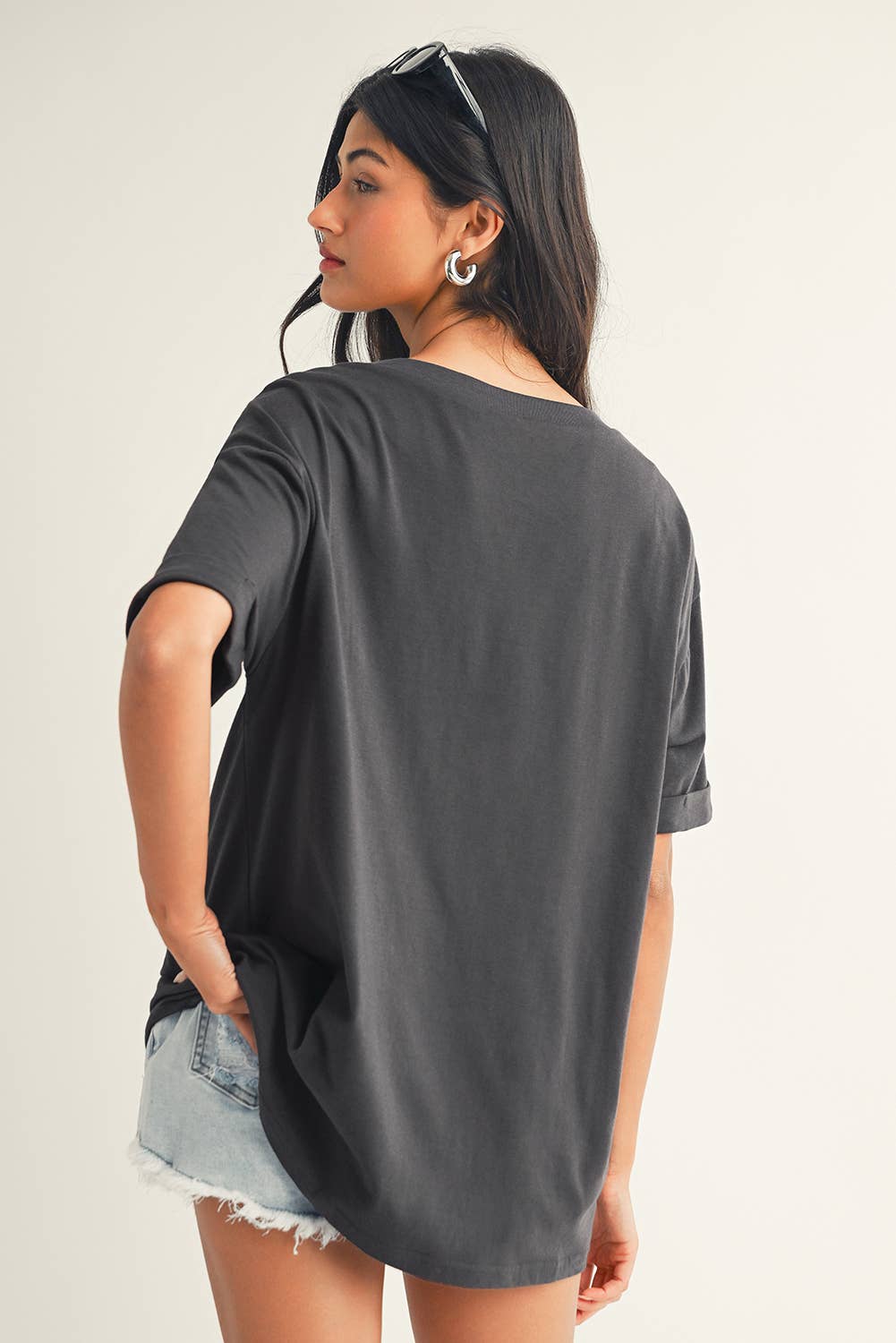 Woman wearing a dark gray oversized t-shirt and denim shorts on a plain background