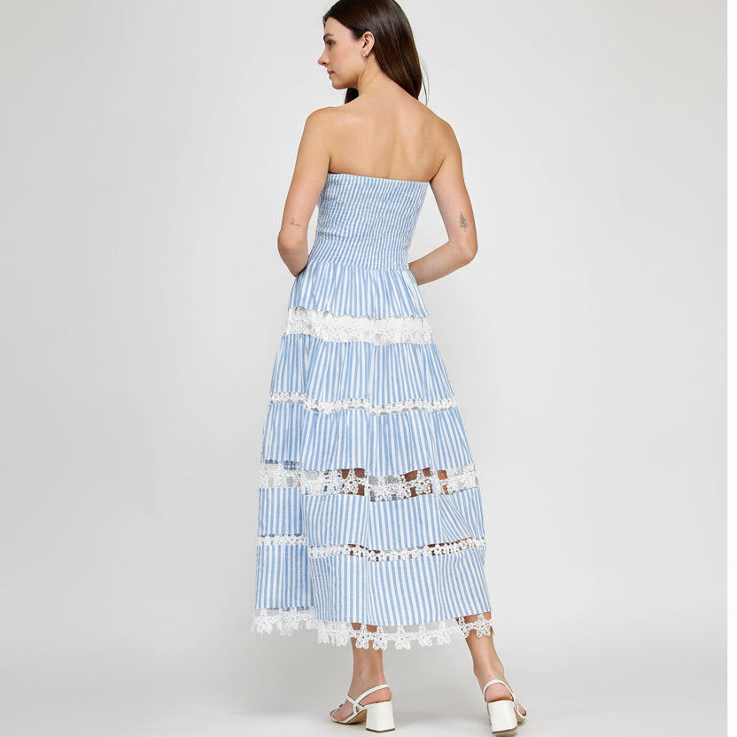 Woman wearing a strapless, light blue and white striped dress with lace details on a white background