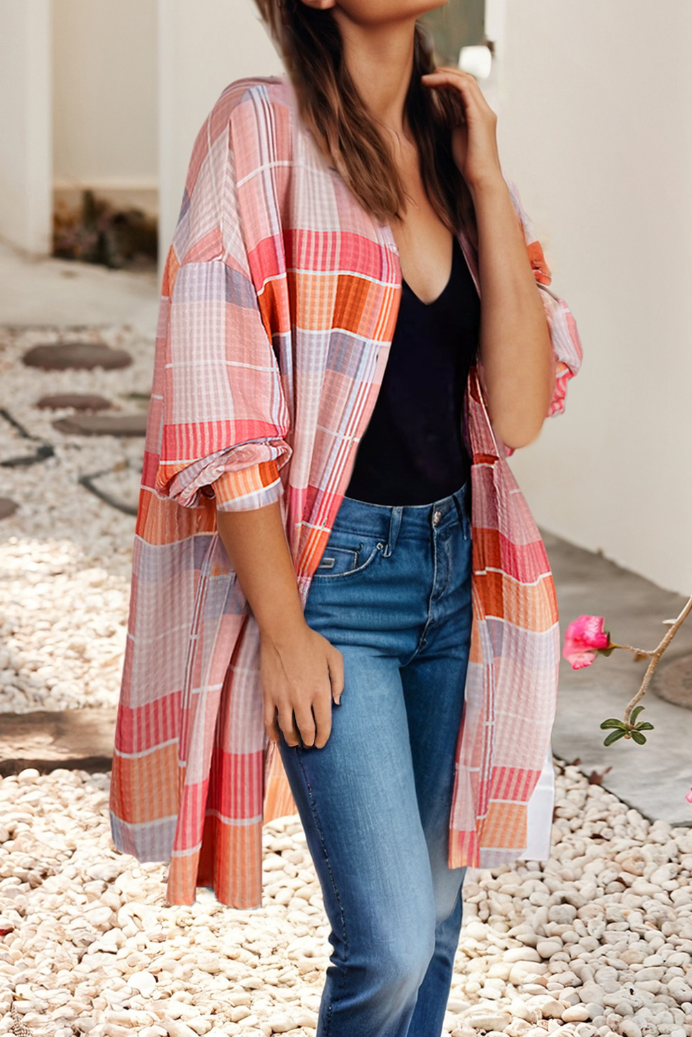 Woman wearing a plaid shirt over a black top and blue jeans on a pebbled surface.