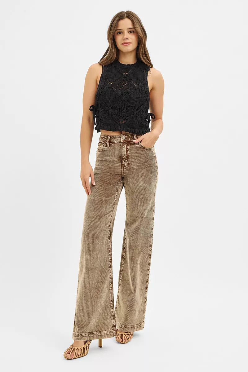 Woman wearing a black sleeveless top and brown flared jeans on a white background
