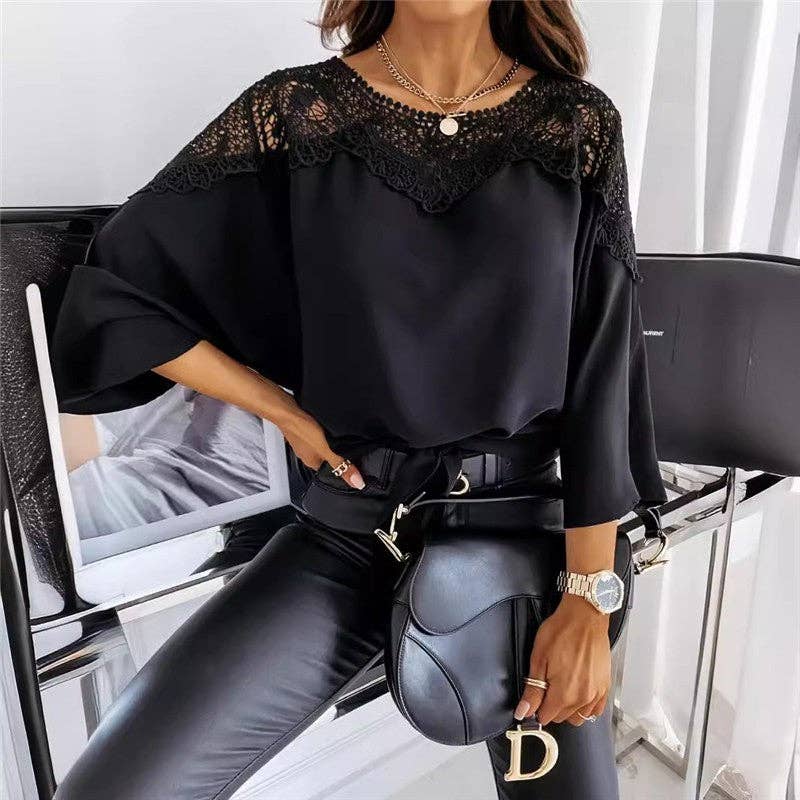 Person wearing a black lace top and black pants with a black handbag, sitting on a chair.