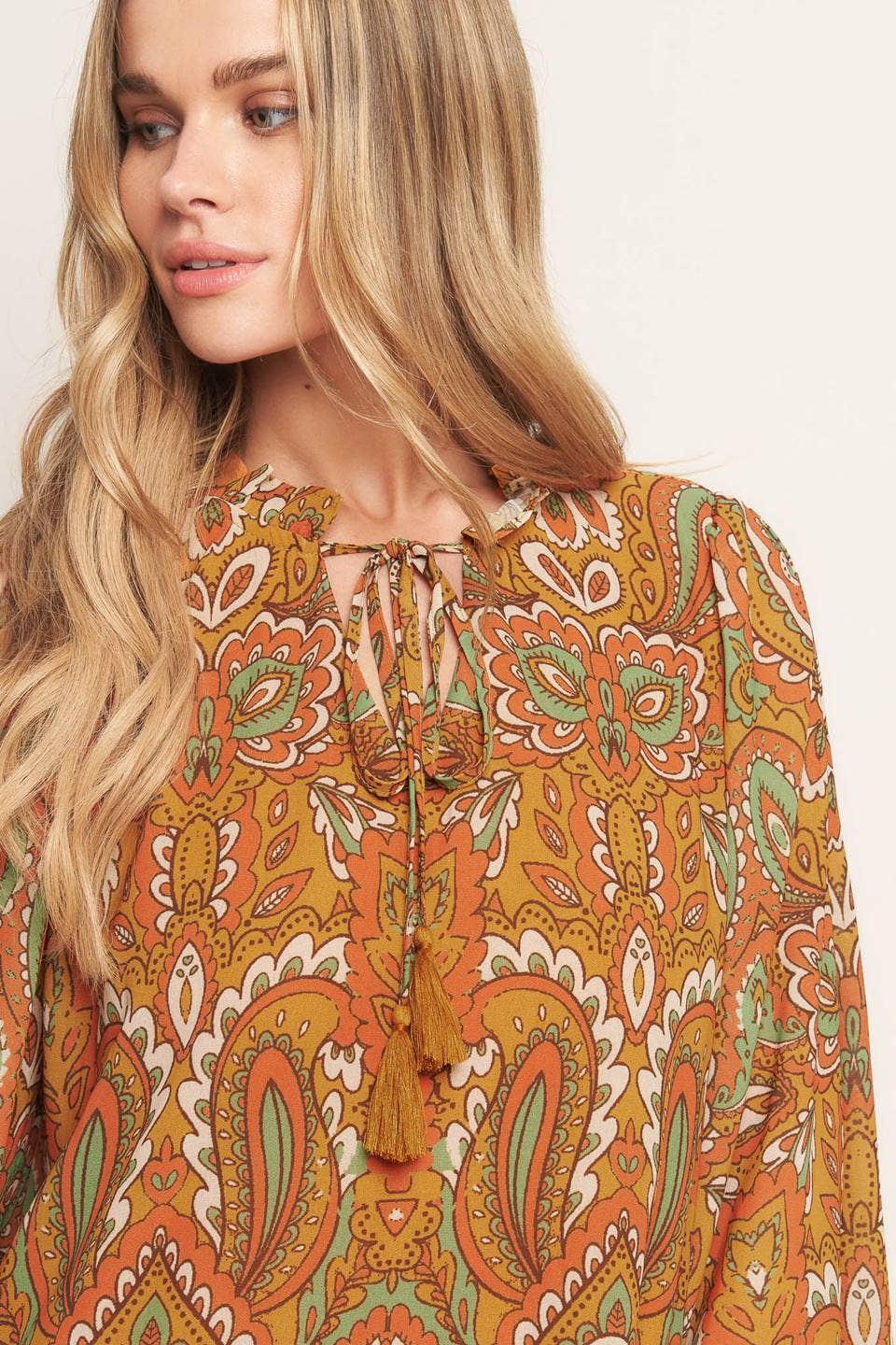 Woman wearing a patterned blouse with orange and green colors on a plain background