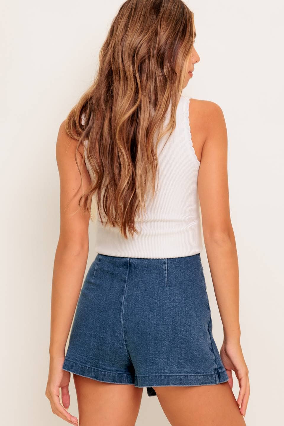 Woman wearing a white tank top and blue denim shorts on a plain background