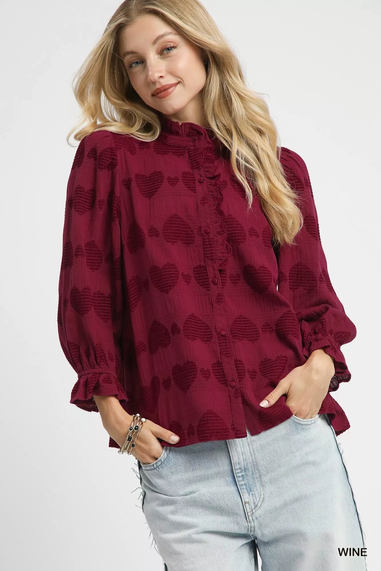 Woman wearing a burgundy blouse with heart patterns and light blue jeans on a white background