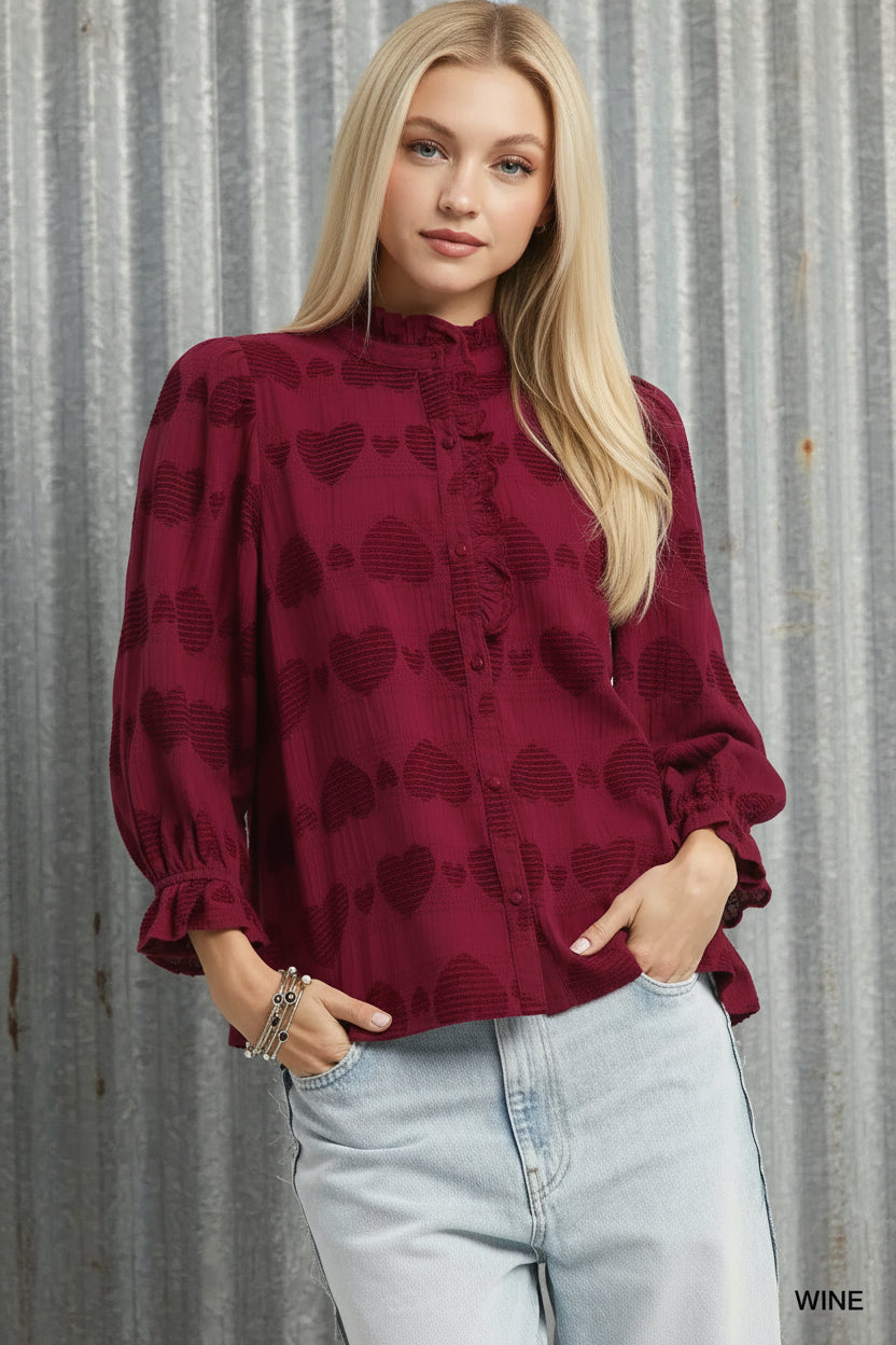 Woman wearing a burgundy blouse with heart patterns and light blue jeans on a white background