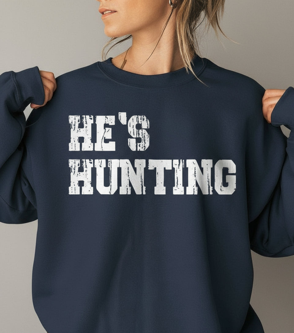 Person wearing a red sweatshirt with 'HE'S HUNTING' text in a bedroom setting