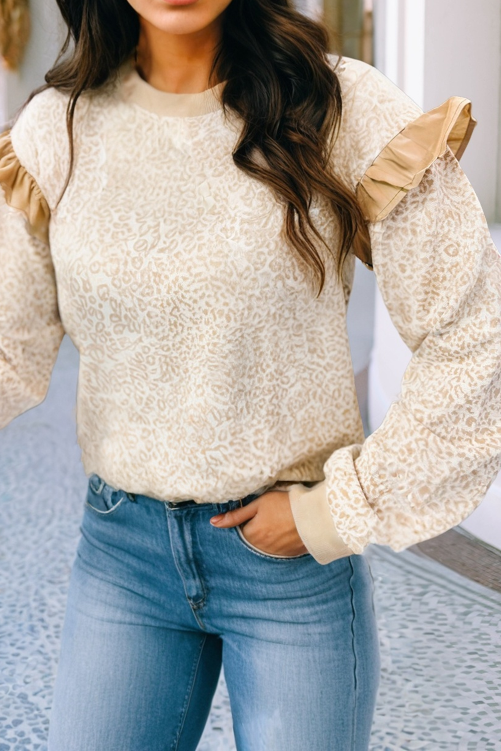 Woman wearing a beige lace top with ruffled sleeves and blue jeans.