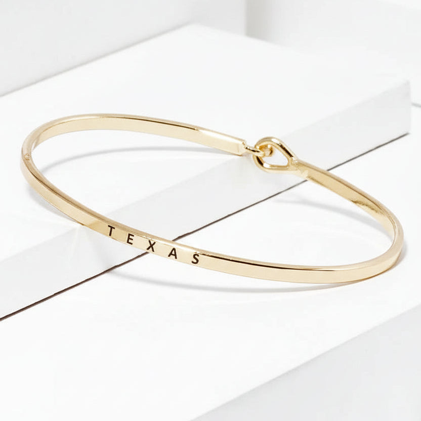Gold bracelet with 'TEXAS' engraving on a white background