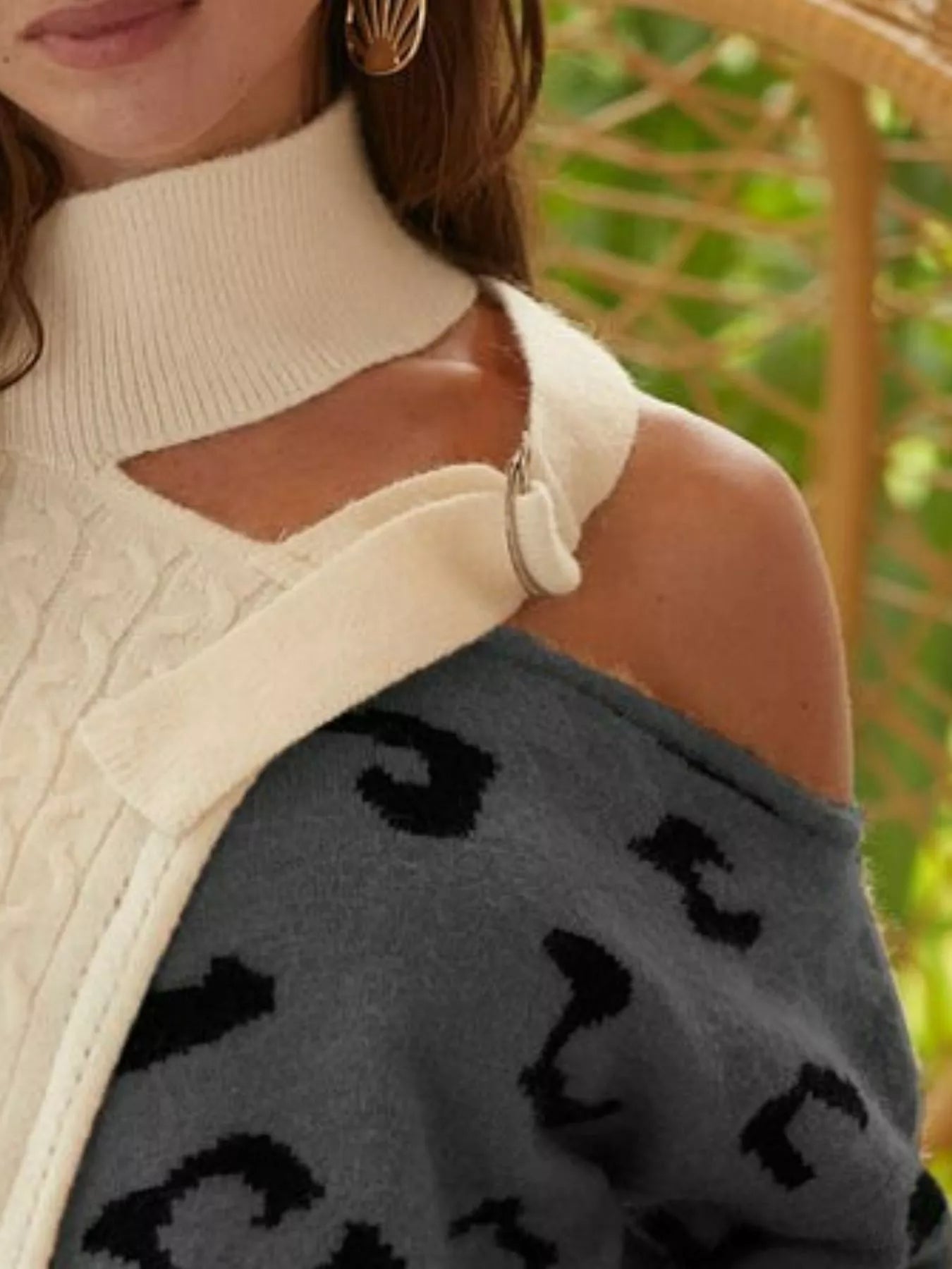 Person wearing a cream sweater with a cut-out design, holding a dark gray sweater with black patterns.