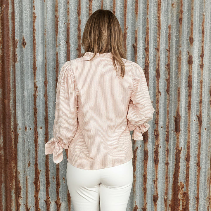 Person wearing a pink striped blouse with long sleeves and a tie detail, standing outdoors.