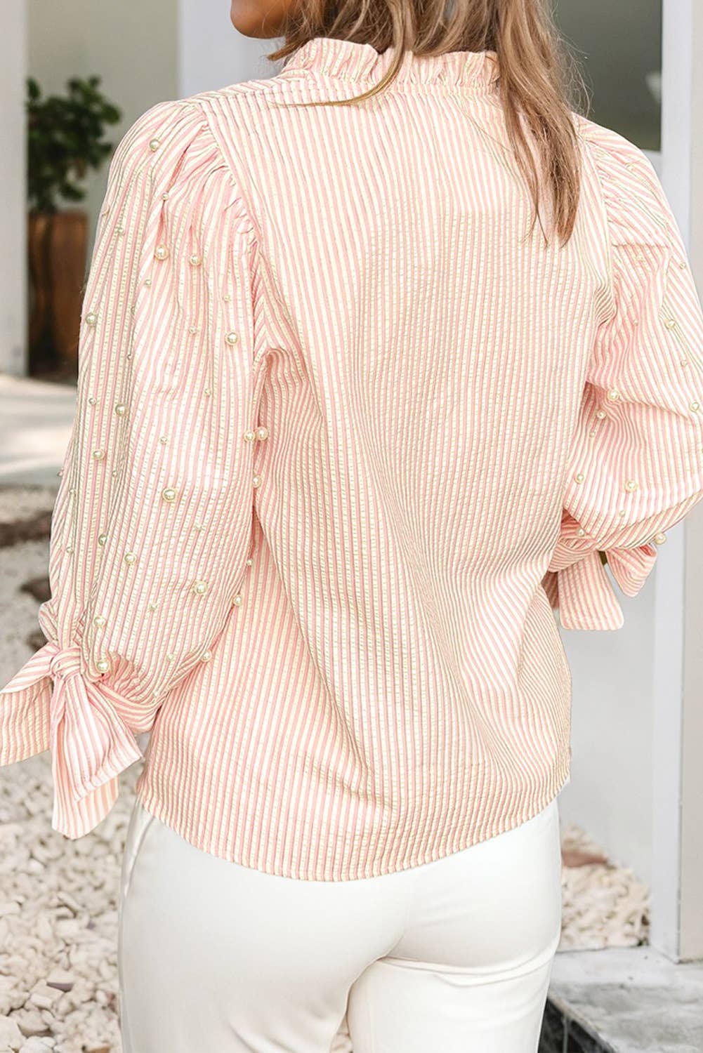 Person wearing a pink striped blouse with long sleeves and a tie detail, standing outdoors.