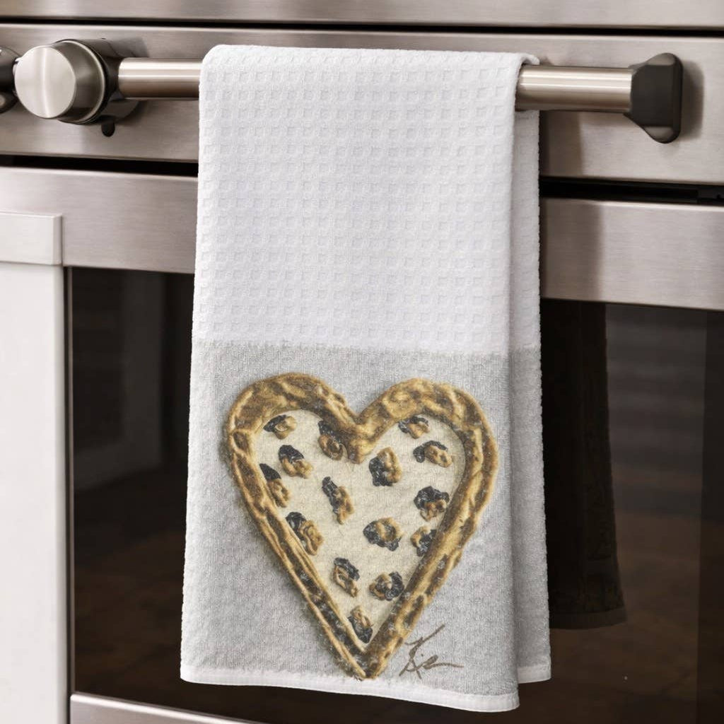 A white kitchen towel with a heart-shaped pizza design hanging from the handle of a stainless steel oven in a kitchen setting.