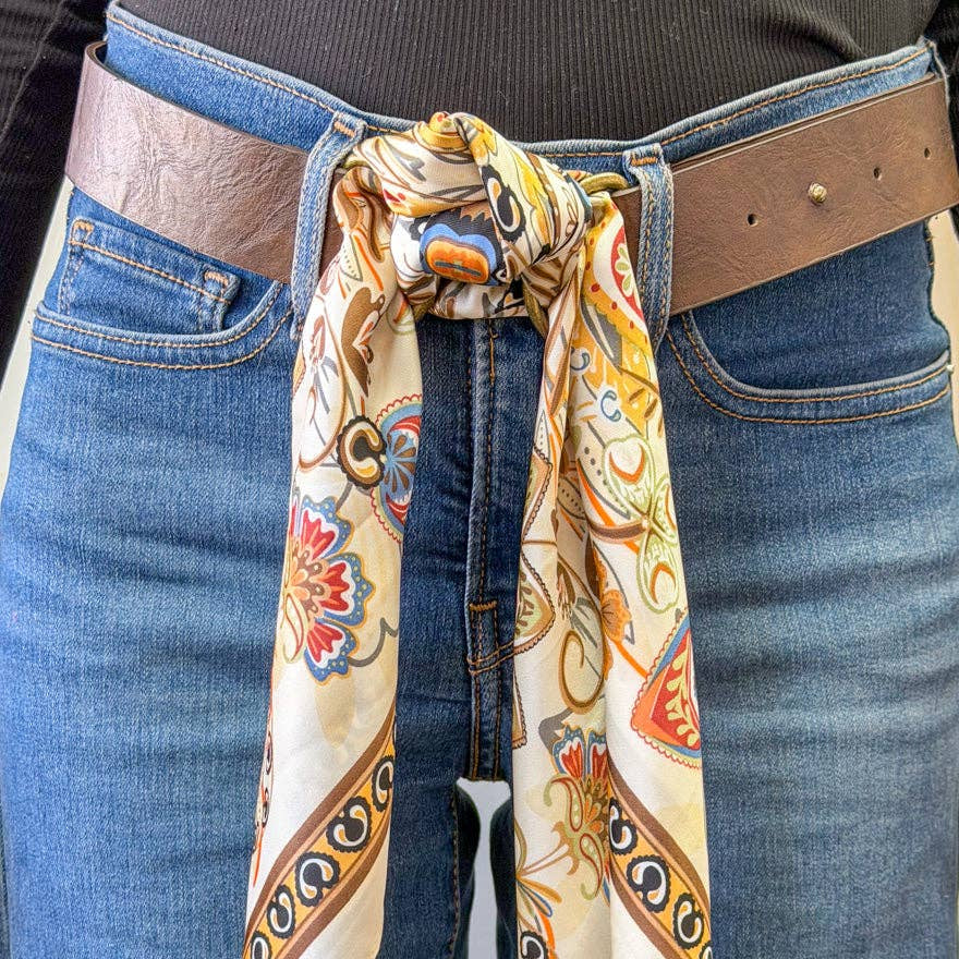Person wearing a patterned scarf tied around their waist with jeans and a brown belt.