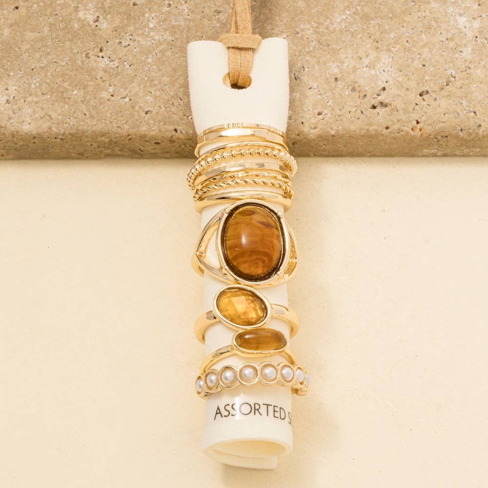 Assorted gold rings displayed on a cylindrical holder against a beige background