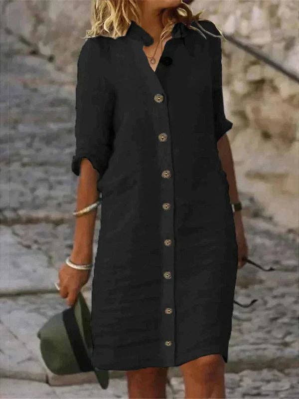 Person wearing a black button-up dress with a blurred stone wall background