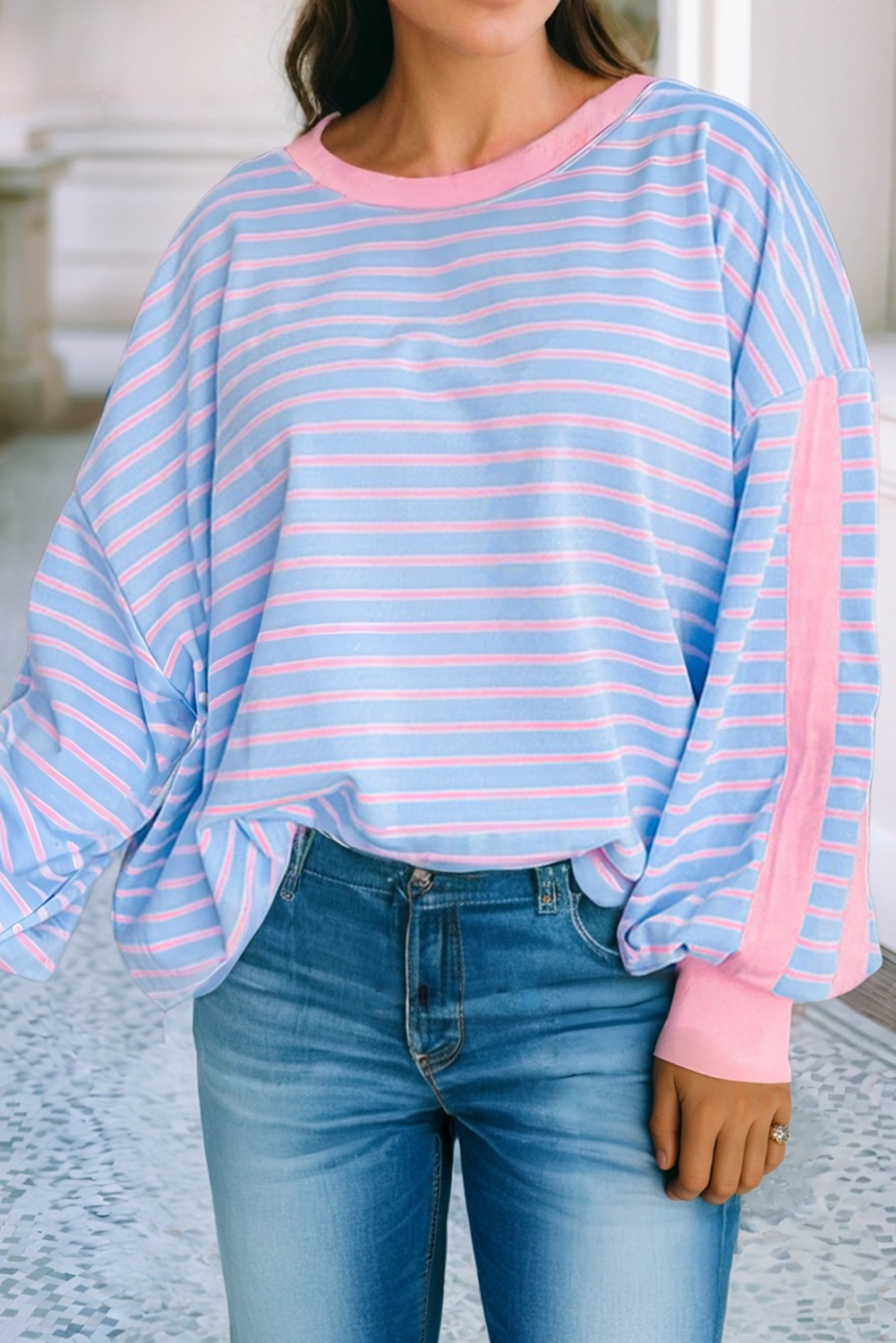 Person wearing a light blue and pink striped sweater with jeans indoors.