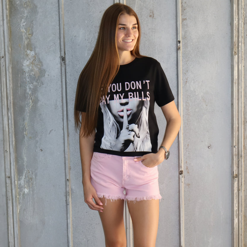 Person wearing a black t-shirt with text and pink shorts standing on a concrete floor.