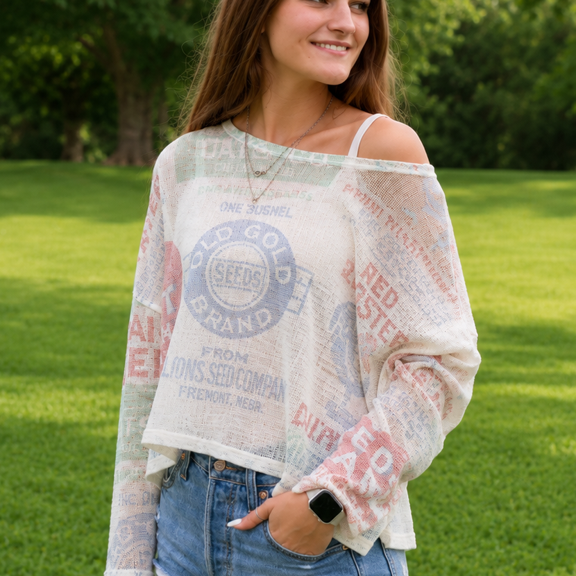 Woman wearing a patterned off-shoulder top and denim shorts standing in a grassy area with trees.