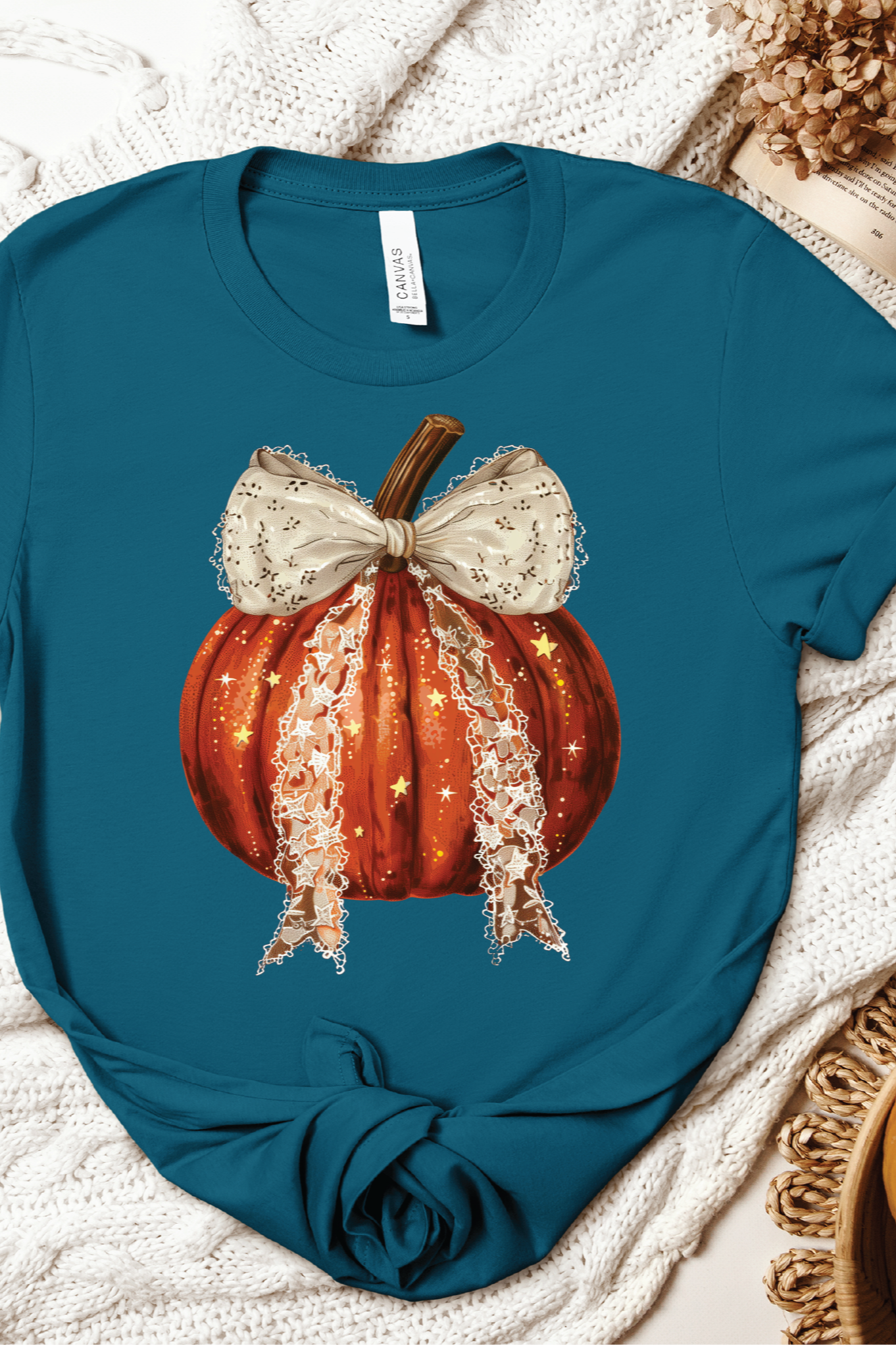 Blue t-shirt with a pumpkin and bow design on a textured surface with pumpkins and leaves.